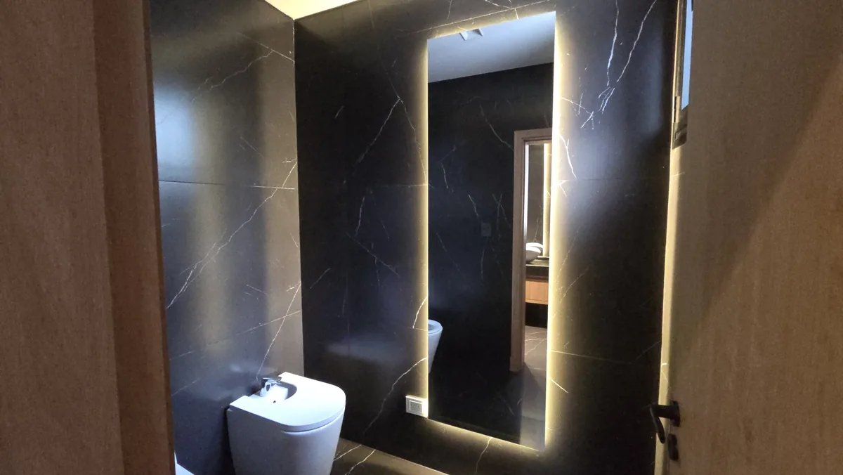 Espejo LED retroiluminado en baño revestido en mármol oscuro - JN Aluminio Neuquén