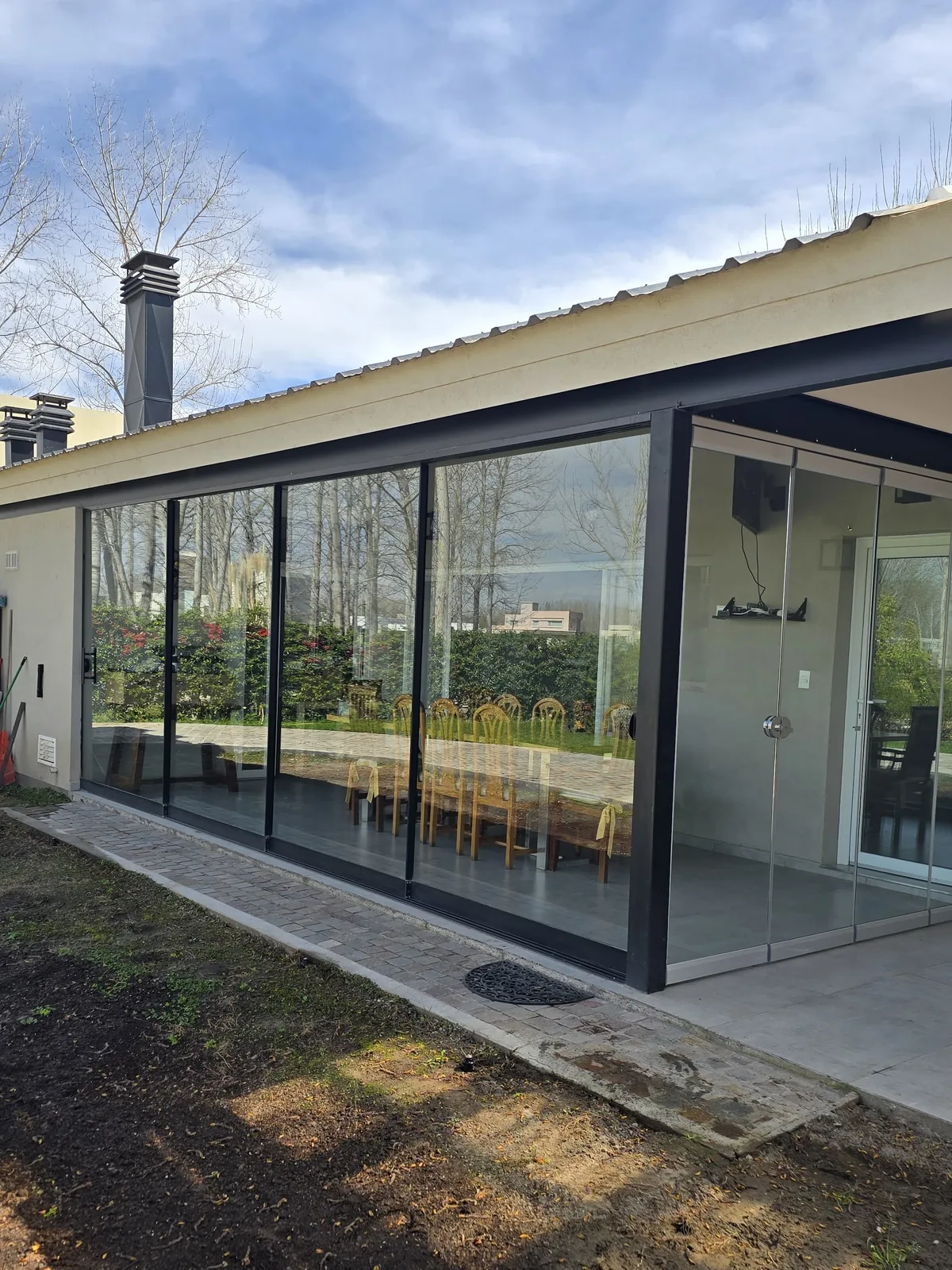 Cerramiento deslizante de vidrio de más de 6 metros con perfilería negra mínima, visto desde el jardín con la casa terminada - obra de J&N Aluminio en Los Canales, Plottier