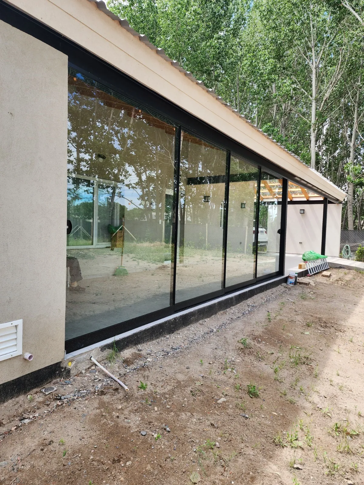 Cerramiento corredizo minimalista de más de 6 metros en vidrio templado, visto desde el jardín - obra de J&N Aluminio en Los Canales, Plottier